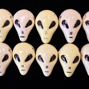 May include: Ten ceramic alien head beads in white and yellow with black painted details. The beads are all the same size and shape, and they have a glossy finish.