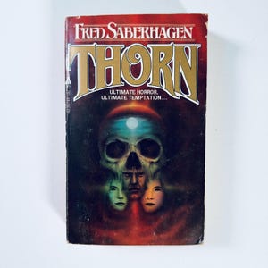 Può includere: Una copertina di un libro tascabile con sfondo rosso e un teschio con una luna sulla fronte. Il titolo "Thorn" è in lettere dorate e l'autore "Fred Saberhagen" è in lettere bianche. Il testo "Ultimate Horror. Ultimate Temptation..." è sotto il titolo.