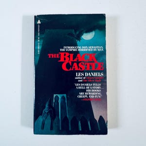 Può includere: Un libro tascabile vintage intitolato "The Black Castle" di Les Daniels. La copertina presenta un'illustrazione oscura e gotica con un pipistrello, una luna piena e il titolo in rosso. Il libro fa parte della serie Ace Fantasy.