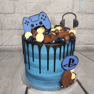 Op de afbeelding: Een blauwe en zwarte dripcake versierd met chocolade snoepjes, een blauwe videogamecontroller en een blauwe en zwarte headset. De cake is bedekt met een blauw en wit PlayStation-logo.