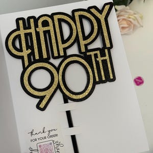 May include: Gold and black glitter cake topper that says "Happy 90th".
