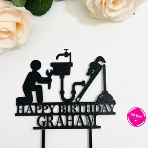 May include: Black cake topper with a silhouette of a plumber holding a wrench and a pipe. The topper says "Happy Birthday Graham".