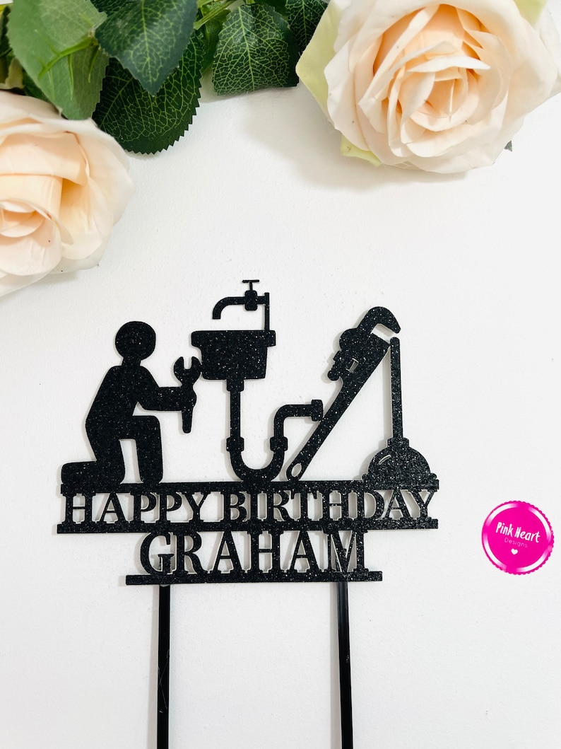 May include: Black cake topper with a silhouette of a plumber holding a wrench and a pipe. The topper says "Happy Birthday Graham".