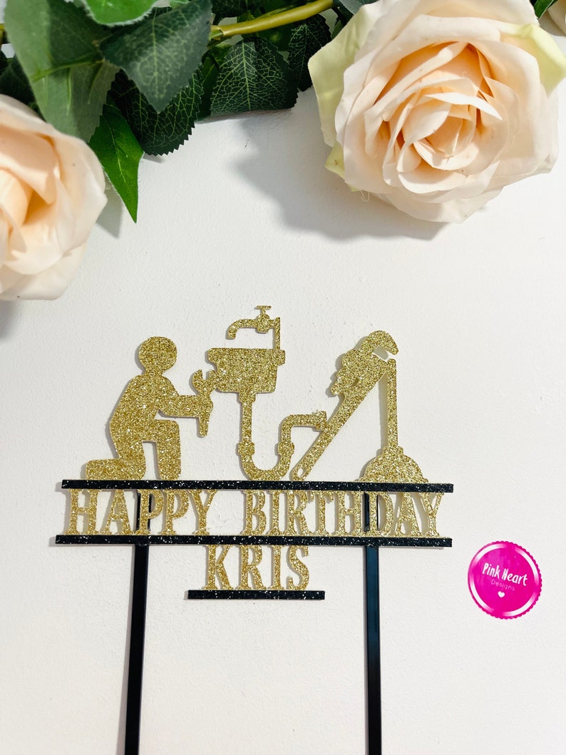May include: Gold glitter cake topper with a plumber silhouette, pipes, and a sink. The topper says "Happy Birthday Kris" on two black banners.