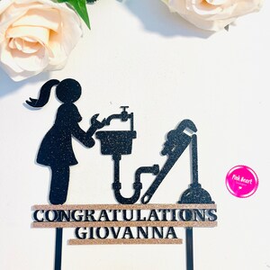 May include: Black glitter cake topper with a silhouette of a woman holding a wrench and a sink. The topper also includes a plunger and a pipe. The text "CONGRATULATIONS GIOVANNA" is on a gold glitter banner.