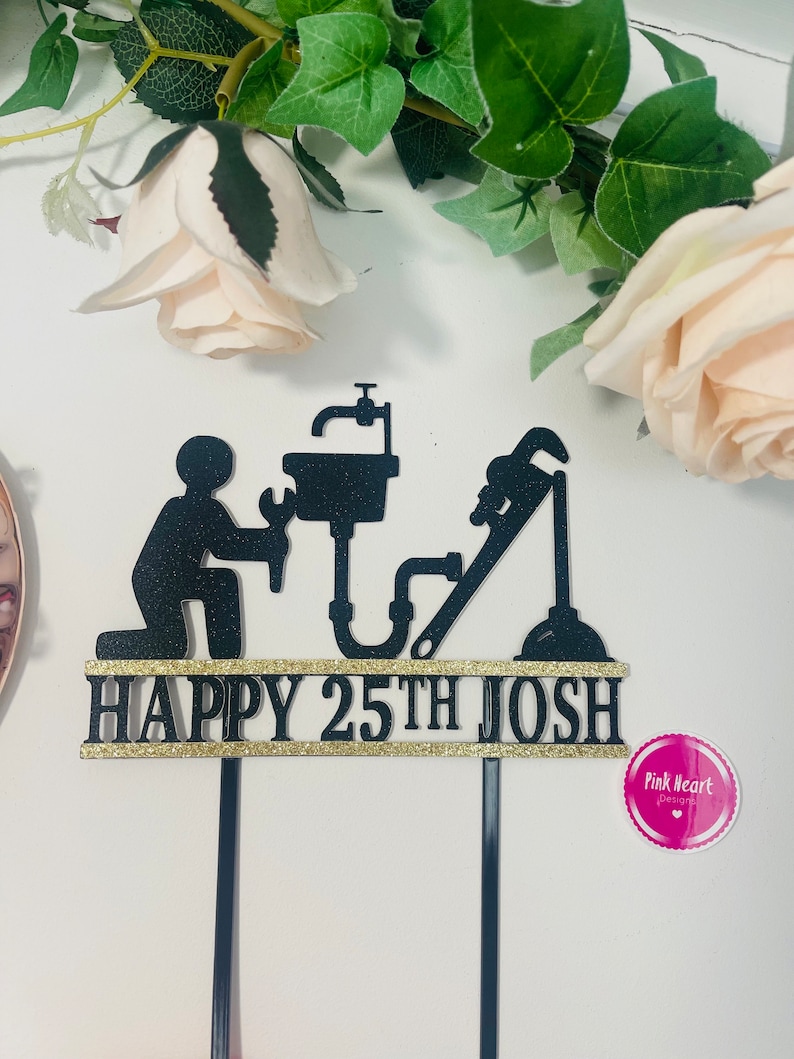 May include: Black cake topper with a silhouette of a plumber holding a wrench and a pipe. The topper says "Happy 25th Josh" in gold glitter.