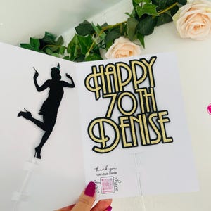 May include: Gold glitter cake topper with the text "Happy 70th Denise". The topper features a black silhouette of a woman in a flapper dress.
