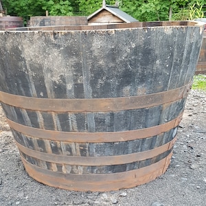 May include: A large, dark wooden barrel planter with metal bands. The barrel is weathered and has a rustic appearance.