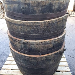 May include: Four stacked wooden barrels, each with a dark brown stain and metal bands. The barrels are weathered and show signs of use.