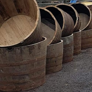 May include: A row of wooden barrels, stacked and arranged in a staggered pattern. The barrels are made of natural wood and have a rustic, weathered appearance. They are ideal for use as planters or decorative elements in a garden or home.