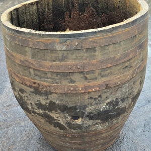 May include: A large, weathered wooden barrel with metal bands. The barrel is dark brown with visible wood grain and a rough interior. The metal bands are rusty and riveted. The barrel's shape tapers towards the base, suggesting it may be a planter.