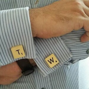 May include: A pair of cufflinks made from wooden Scrabble tiles. The tiles are light brown and have the letters "T." and "W." printed on them in black.