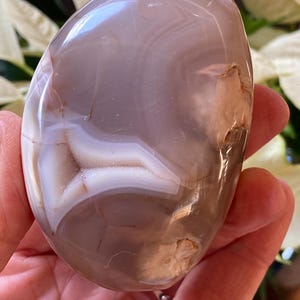 May include: A smooth, polished agate stone with a light brown, white, and gray banded pattern. The stone is shaped like an oval and has a glossy finish.