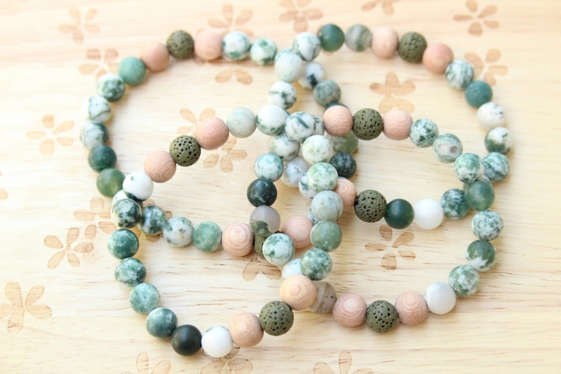 May include: Three bracelets made of green, white, and brown beads. The bracelets are made of different materials, including wood, lava rock, and agate.