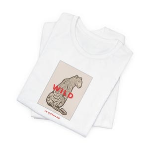May include: White t-shirt featuring a graphic of a leopard with the word "WILD" in red. The leopard is in a beige rectangle with the text "LE GUÉPARD" below. The shirt is folded.
