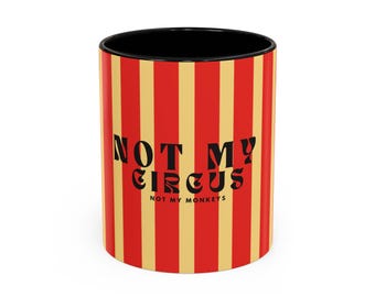 Op de afbeelding: Een rood-gele gestreepte keramische mok met zwarte tekst die "Not My Circus, Not My Monkeys" luidt.