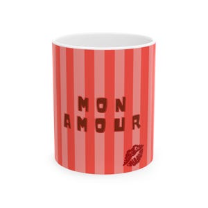May include: A white ceramic mug with a red and light red striped pattern. The mug features the words "MON AMOUR" in brown letters and a red lip print. The mug is cylindrical and has a white interior.