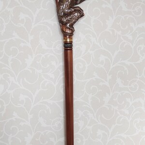 May include: A wooden walking stick with a carved monkey figure at the top. The monkey is brown and is holding onto a branch. The stick is brown and has a black rubber tip.