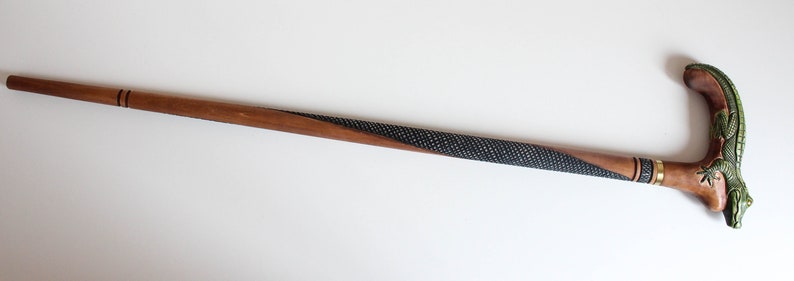 May include: A wooden walking stick with a carved green lizard handle. The stick is brown with a black and white patterned section.