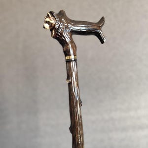 May include: A wooden walking stick with a carved raccoon head at the top. The stick has a brown finish and a gold band near the top.