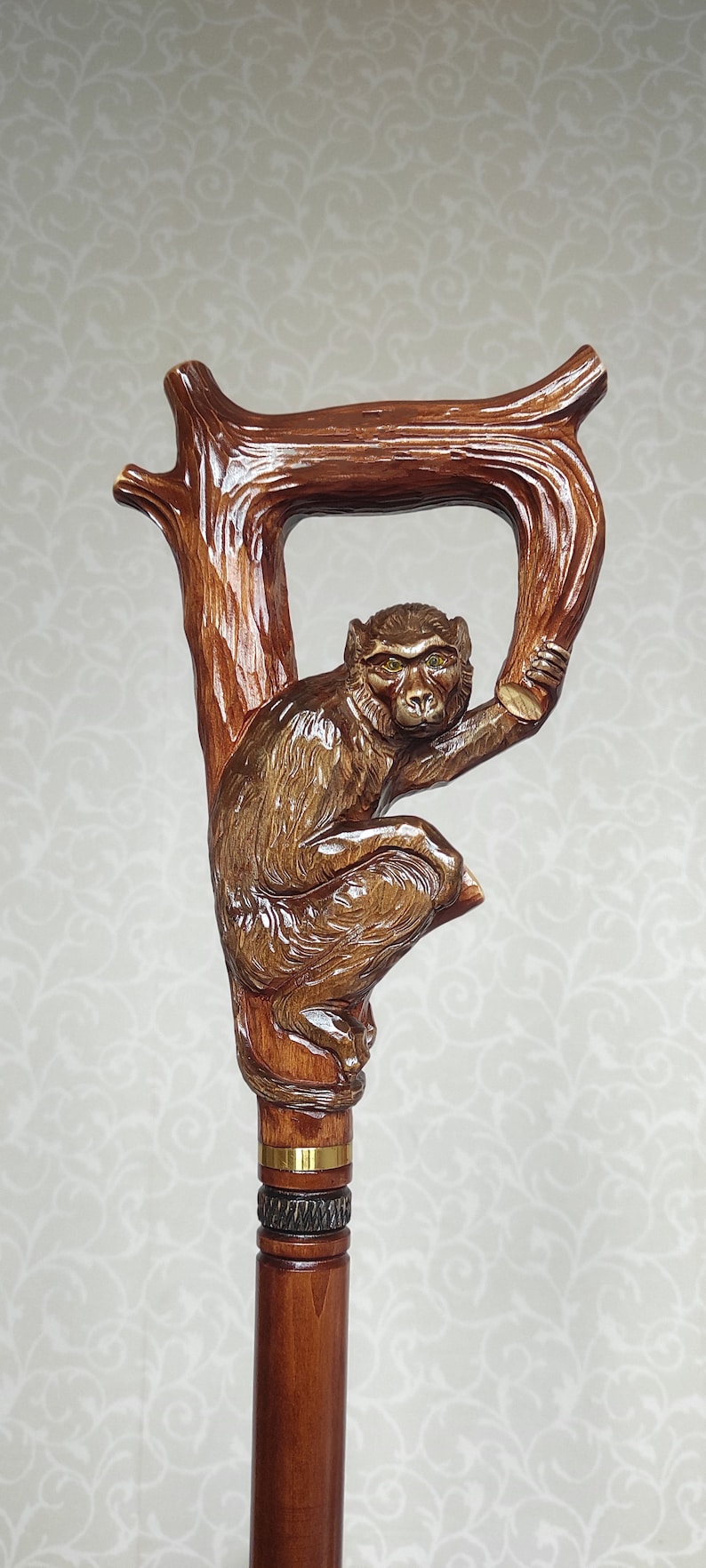 May include: A wooden walking stick with a carved monkey holding onto a branch. The monkey has brown fur and yellow eyes. The stick is brown and has a gold band around it.
