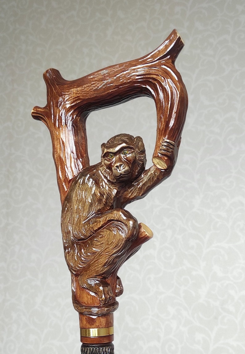 May include: A wooden walking stick with a carved monkey holding onto a branch. The monkey has brown fur and green eyes.