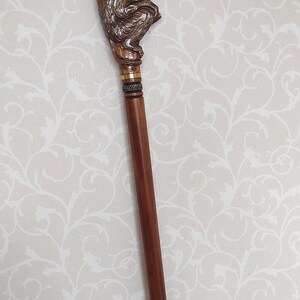 May include: A wooden walking stick with a carved monkey figure at the top. The monkey is brown and sitting on a branch. The stick is brown and has a black rubber tip.