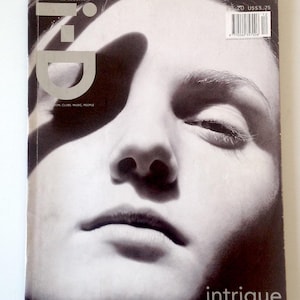 Pode incluir: Uma capa de revista a preto e branco com um close-up de um rosto. A revista "i-D" é visível, juntamente com o texto "THE OUTRAGE ISSUE NO. 171" e a palavra "intrigue". A capa tem uma estética vintage.