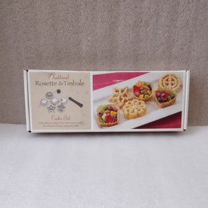 May include: A white box set labeled "Traditional Rosette & Timbale Cookie Set" with images of cookie molds and finished cookies. The set includes a variety of shapes, and the cookies are filled with fruit.