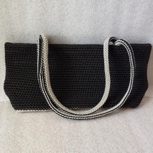 May include: Black crochet tote bag with white trim on the straps.