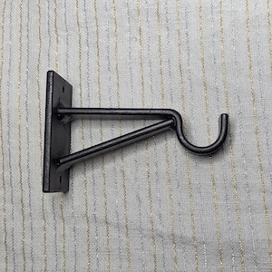 May include: Black metal wall mounted hook with a curved arm. The hook is designed to hold a variety of items, such as coats, hats, or bags.