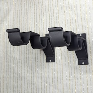 May include: Two black metal curtain rod brackets with a decorative scroll design. The brackets are mounted to a wall.