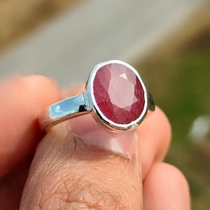 May include: A silver ring with a red oval gemstone. The ring is set in a simple band and the gemstone is faceted.