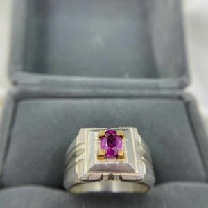 May include: A silver ring with a square setting and a pink oval gemstone. The ring has gold accents around the gemstone.