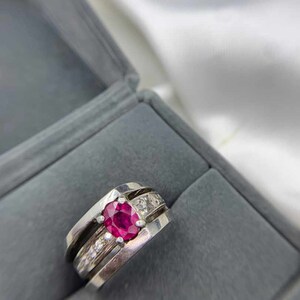 Può includere: Un anello d'argento con una pietra preziosa di rubino rosso circondata da piccole pietre bianche.