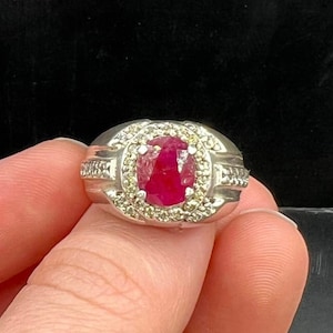 May include: A silver ring featuring a large oval ruby gemstone set within a halo of smaller diamonds.