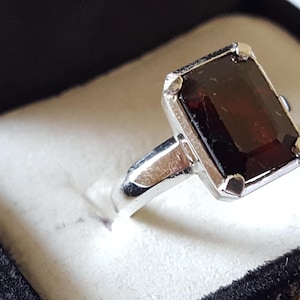May include: A silver ring with a dark red rectangular gemstone.