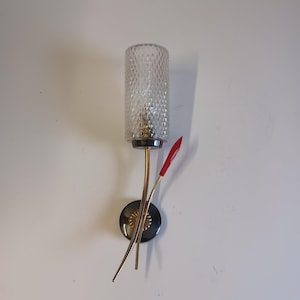 May include: A vintage wall sconce with a clear, diamond-patterned glass shade. The sconce has a gold-toned metal frame, a black base, and a red accent. The design is reminiscent of mid-century modern decor.