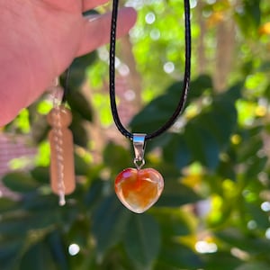 May include: A heart-shaped carnelian pendant on a black cord necklace. The pendant is a light orange color with red and yellow streaks.