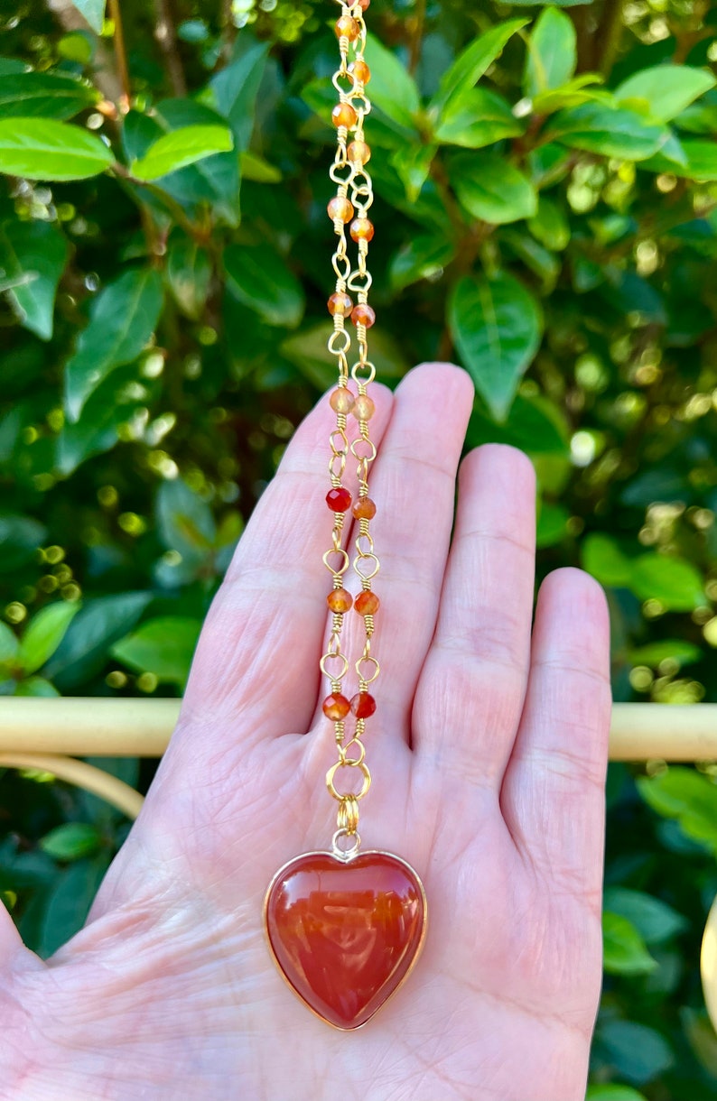 May include: A gold chain necklace with carnelian beads and a large carnelian heart pendant.
