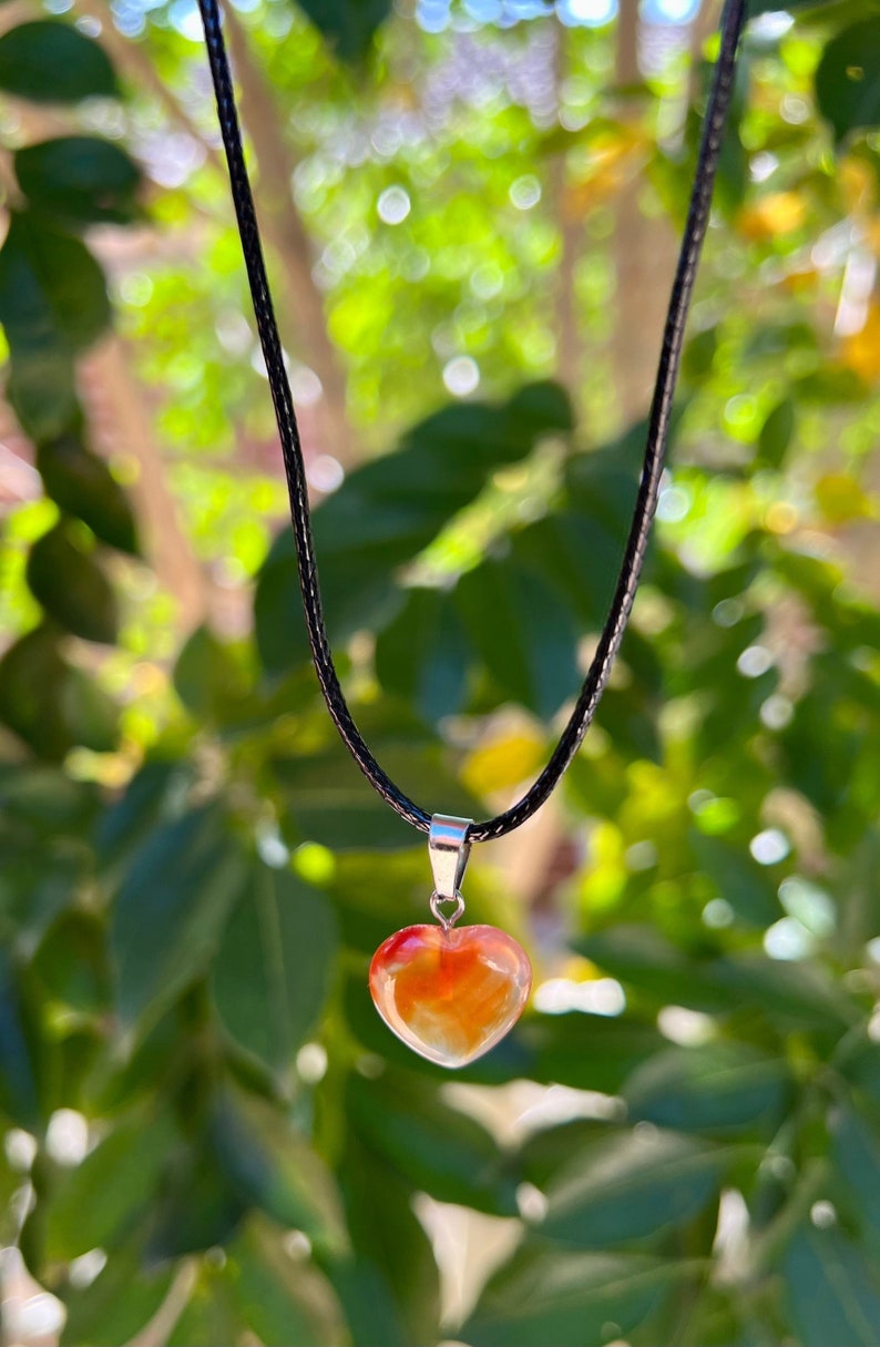 May include: A heart-shaped carnelian pendant on a black cord necklace. The carnelian is a deep orange color with red and yellow streaks.