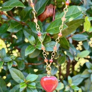 May include: A gold chain necklace with carnelian beads and a red carnelian heart pendant.