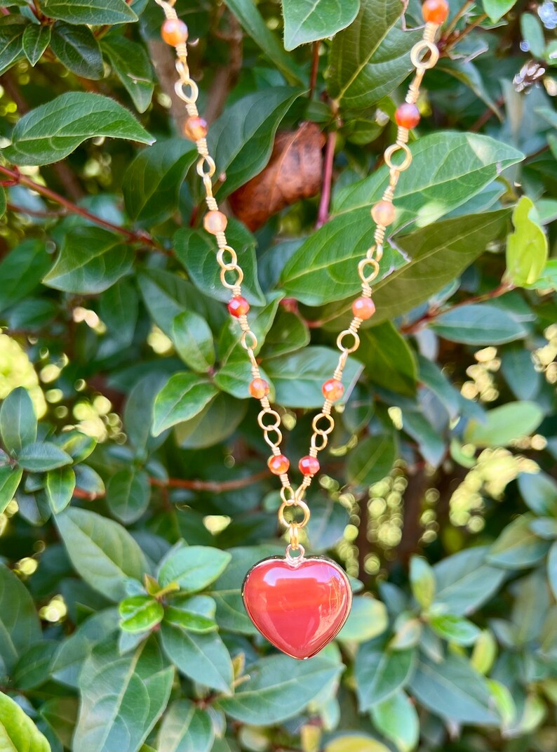 May include: A gold chain necklace with carnelian beads and a red carnelian heart pendant.
