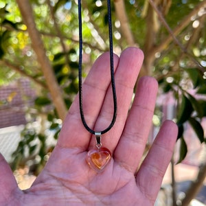 May include: A heart-shaped pendant necklace with a clear, orange, and yellow crystal on a black cord.