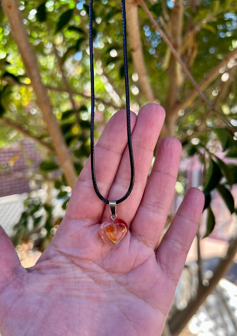 May include: A heart-shaped pendant necklace with a clear, orange, and yellow crystal on a black cord.