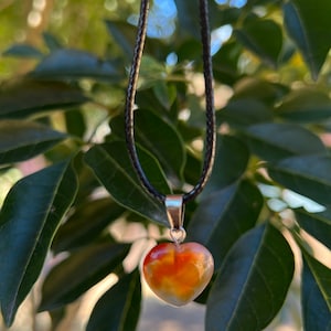 May include: A heart-shaped carnelian pendant necklace on a black cord. The carnelian is a deep orange color with white and brown streaks.