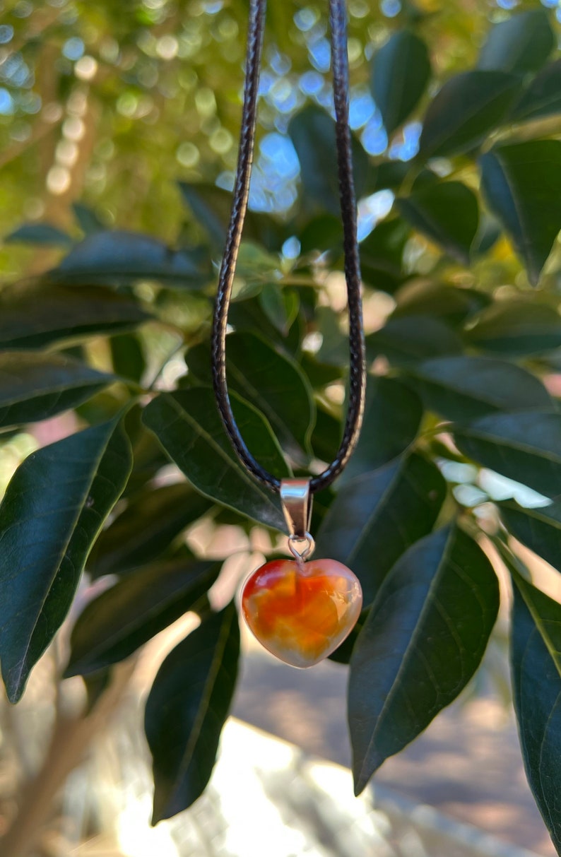 May include: A heart-shaped carnelian pendant necklace on a black cord. The carnelian is a deep orange color with white and brown streaks.