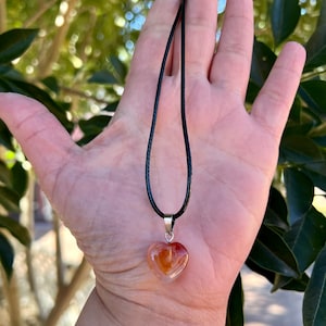 May include: A heart-shaped carnelian pendant necklace on a black cord. The pendant is a light orange color with darker orange and white streaks.