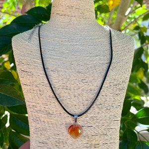 May include: A heart-shaped carnelian pendant necklace on a black cord. The pendant is a natural stone with orange, red, and white hues.