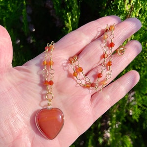 May include: A gold chain necklace with carnelian beads and a large carnelian heart pendant.